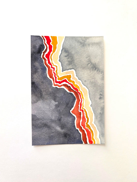 A vertical watercolor art print featuring a jagged, layered diagonal line in red, orange, yellow, and white cutting through a gray and charcoal watercolor background, displayed against a clean white wall.