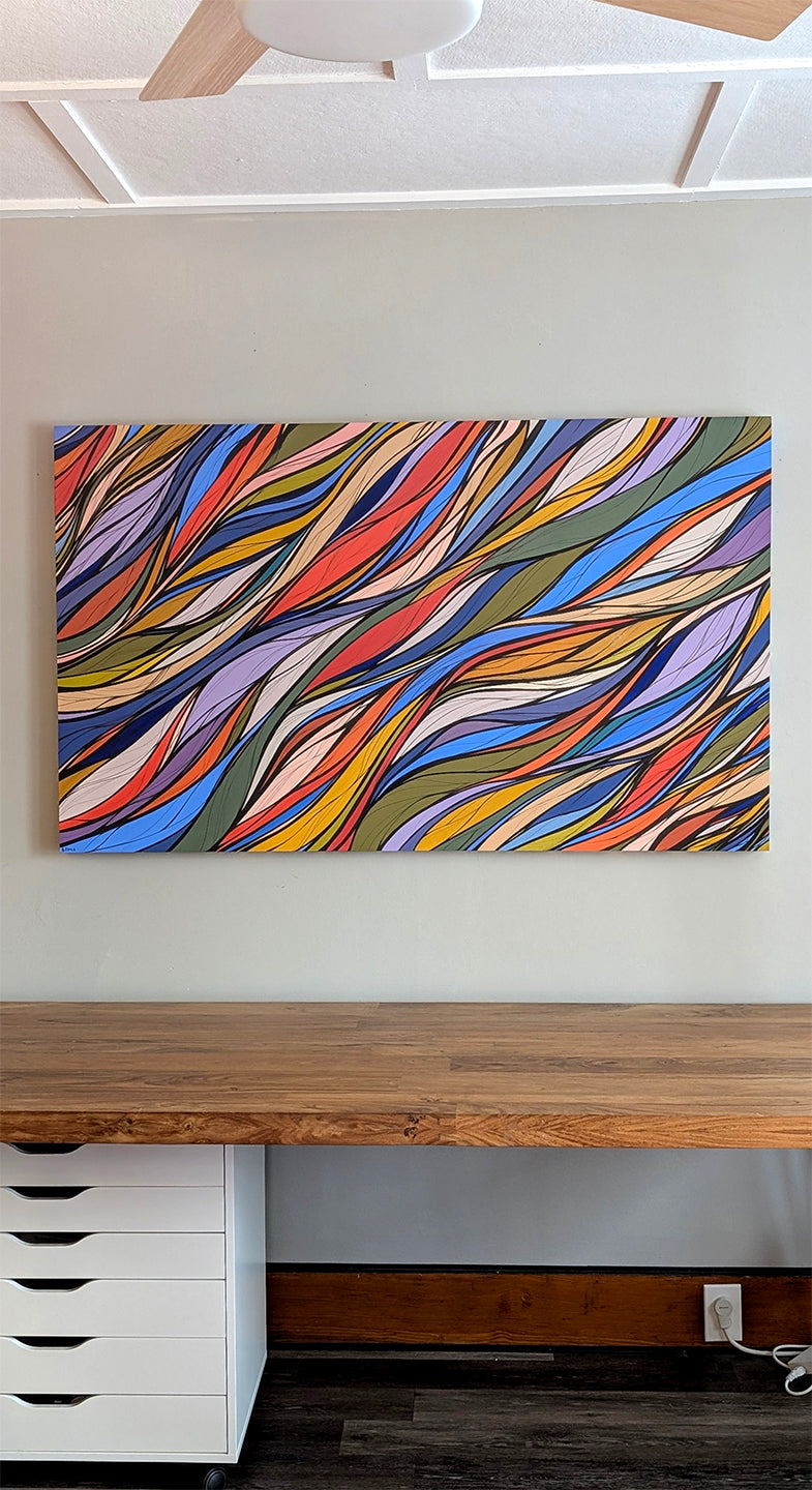 A colorful abstract original painting with flowing wavy lines in red, orange, yellow, green, blue, purple, and white, displayed on a light gray wall above a wooden desk. Resonance Painting by Briana Feola